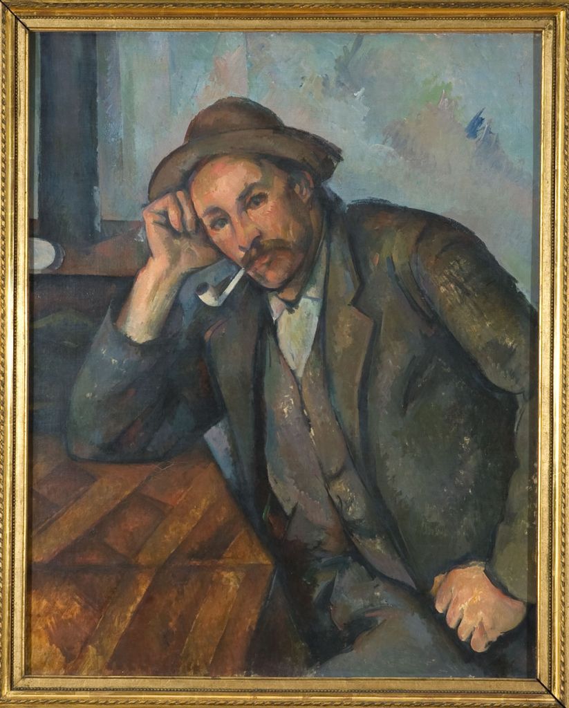 Das Gemälde zeigt das Porträt eines Mannes mit Hut. Er hat seinen rechten Arm auf einem Tisch vor ihm aufgestützt und seinen Kopf in die rechte Hand gelehnt. Sein Blick führt aus dem Bild in Richtung der Betrachter*innen.