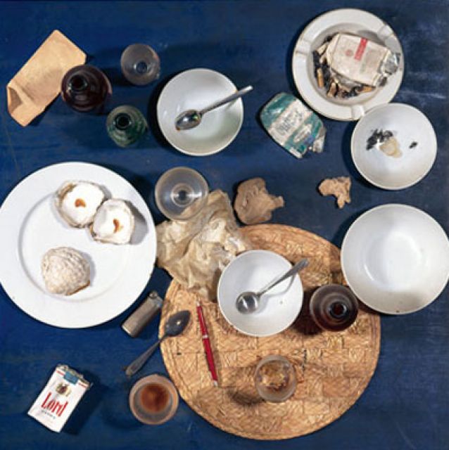 Das quadratische Werk "Ein Tisch aus dem Restaurant Spoerri" besteht aus einer blauen hölzernen Tischplatte, auf der Reste eines Mahls befestigt wurden - etwa Schüsseln, Teller, Brotreste, Löffel, Aschenbecher mit ausgedrückten Zigaretten, ein Feuerzeug.